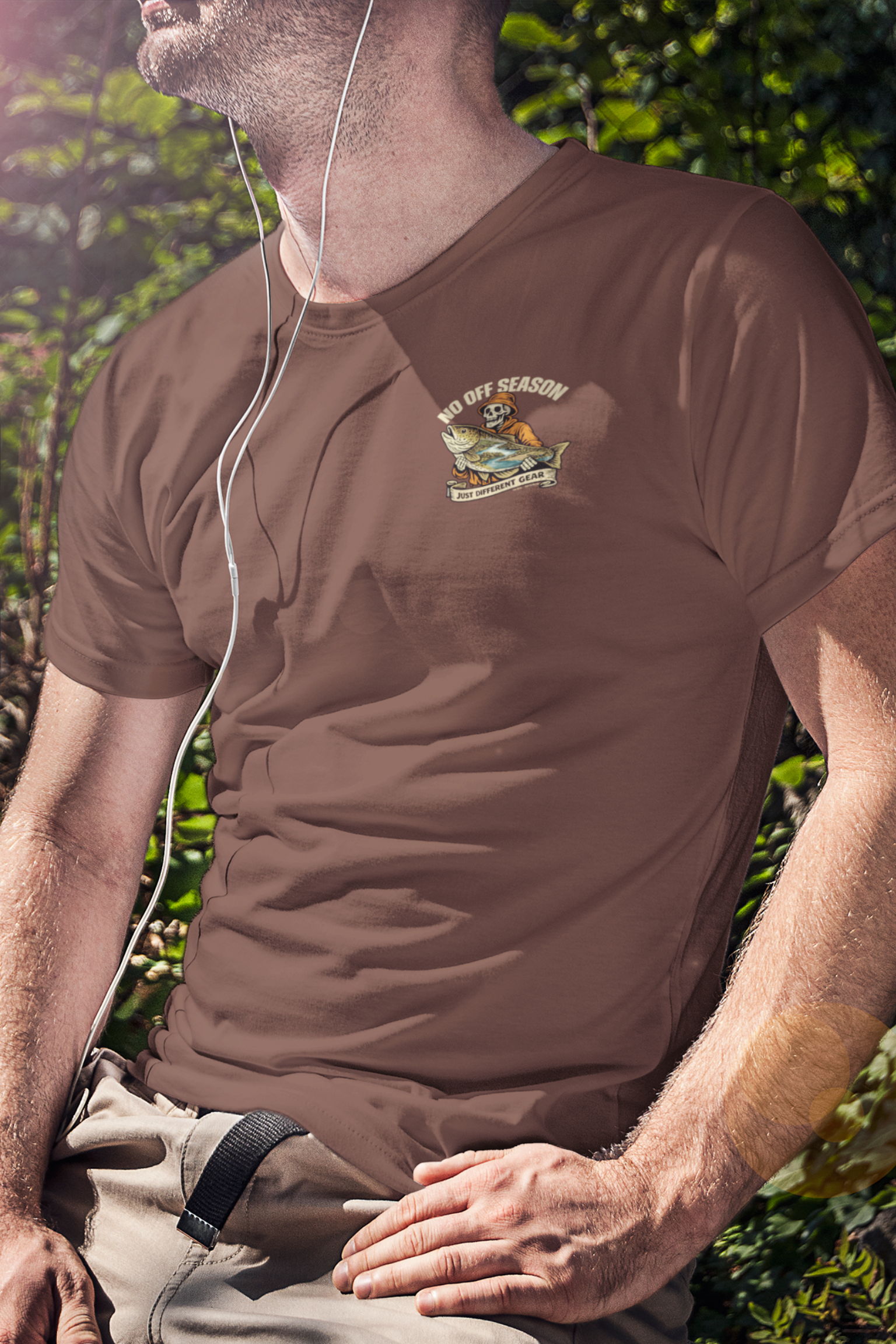 Man wearing a brown t-shirt with No Off Season Last Cast Graphic, sitting outdoors.